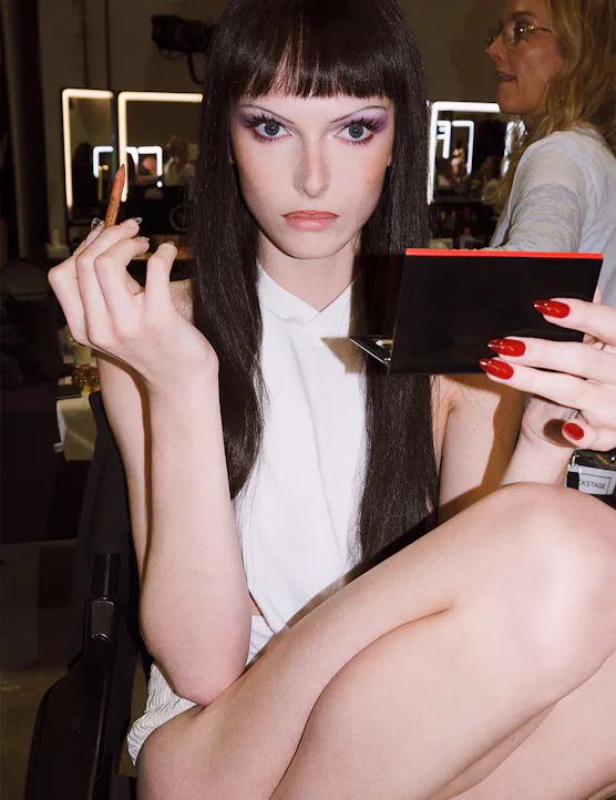 alex consani in a brunette wig putting on makeup