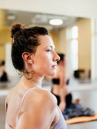 Side profile of a sweaty young woman in a sports bra with hair in a bun, looking focused in a bright...