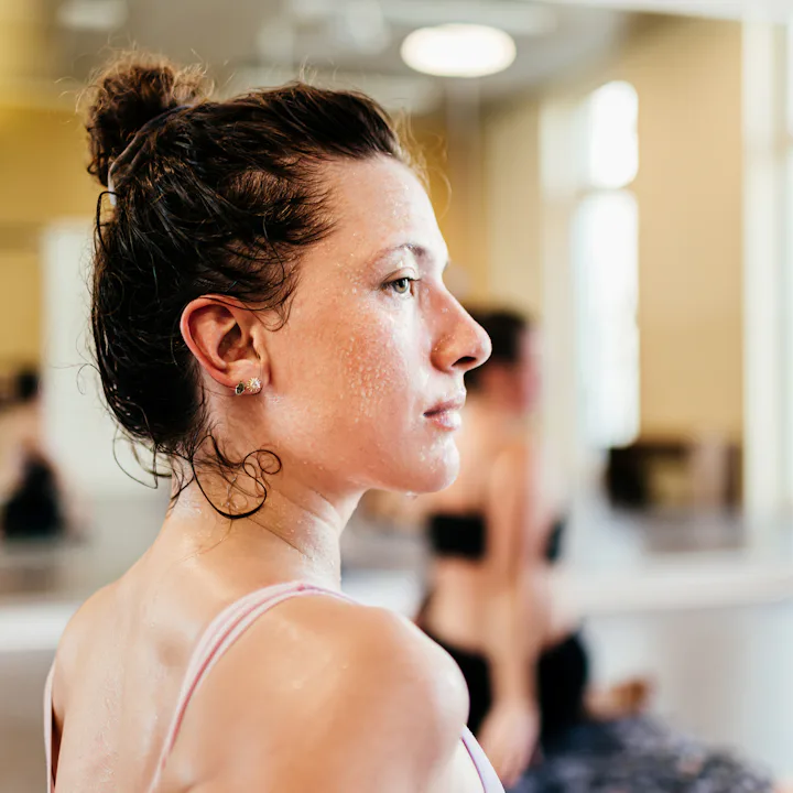 Side profile of a sweaty young woman in a sports bra with hair in a bun, looking focused in a bright...