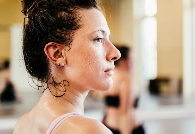 Side profile of a sweaty young woman in a sports bra with hair in a bun, looking focused in a bright...
