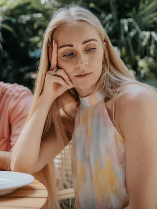 Two adults sitting at an outdoor table with empty plates, both looking away and appearing distant or...