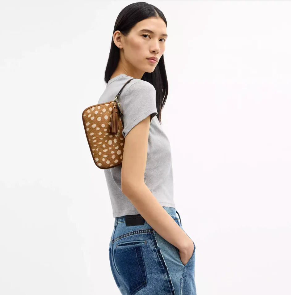 Model wearing the Coach Nolita 19 shoulder bag in deer print over her shoulder