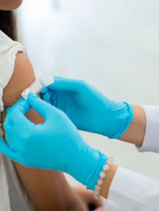 Healthcare worker in blue gloves preparing a bandage on a young person's upper arm after a vaccine o...