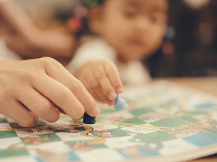 Close-up of an adult and a child moving game pieces on a colorful board game, hands in focus while t...