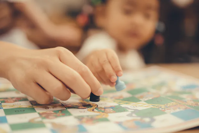 Close-up of an adult and a child moving game pieces on a colorful board game, hands in focus while t...