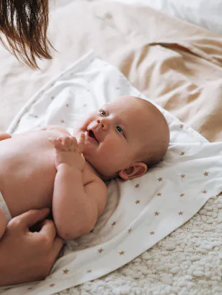 A parent leans over a newborn baby lying on a star-patterned blanket on a bed, the diapered infant g...