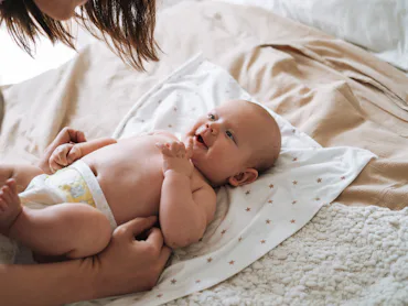 A parent leans over a newborn baby lying on a star-patterned blanket on a bed, the diapered infant g...