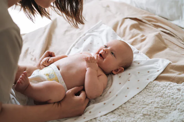 A parent leans over a newborn baby lying on a star-patterned blanket on a bed, the diapered infant g...
