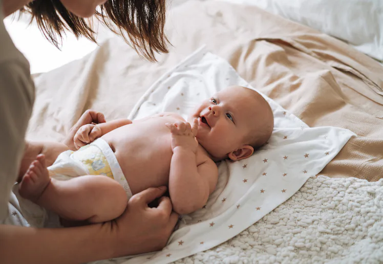 A parent leans over a newborn baby lying on a star-patterned blanket on a bed, the diapered infant g...