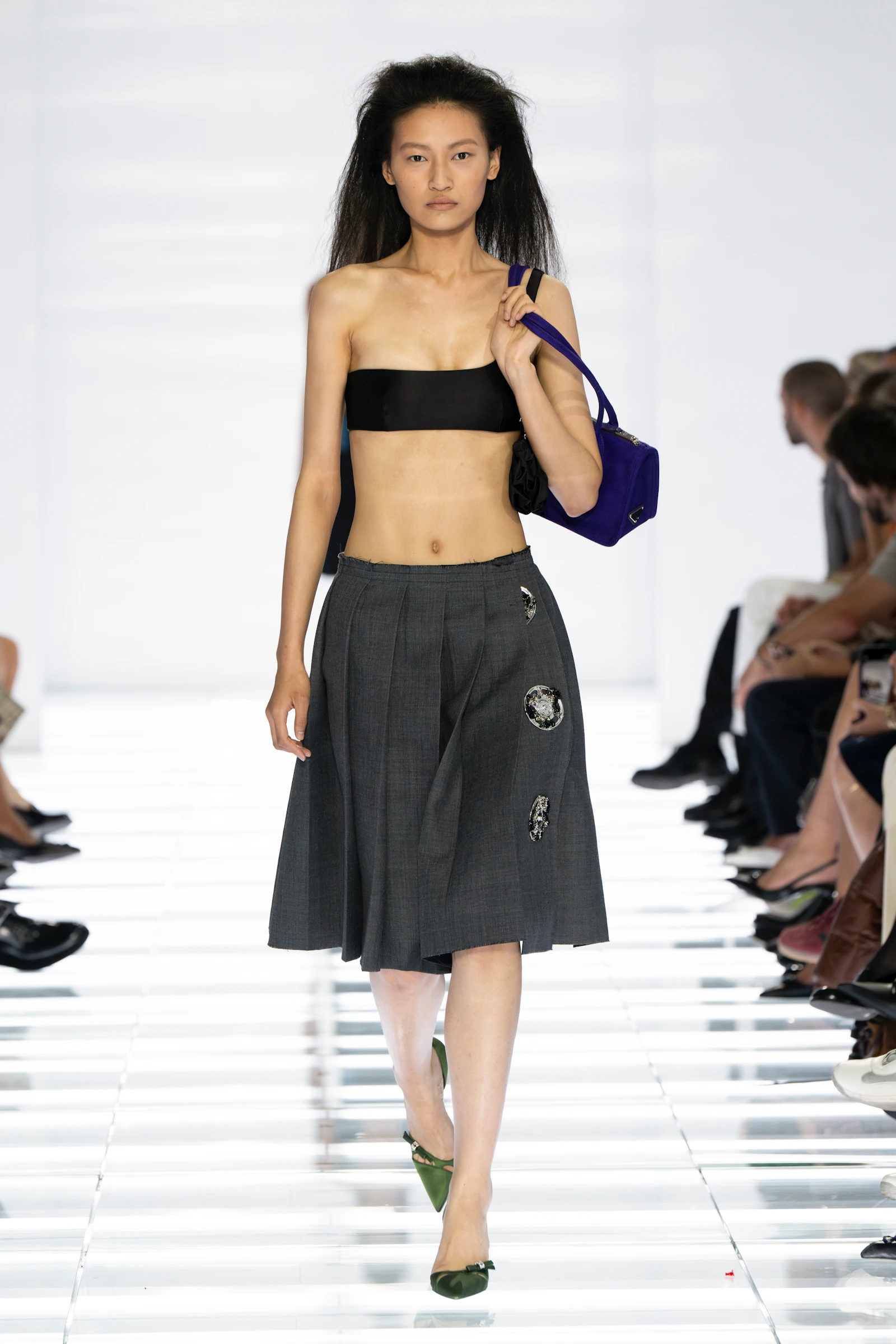 Model in a black Prada bandeau and grey raw-edged kilt skirt with jewelled hardware