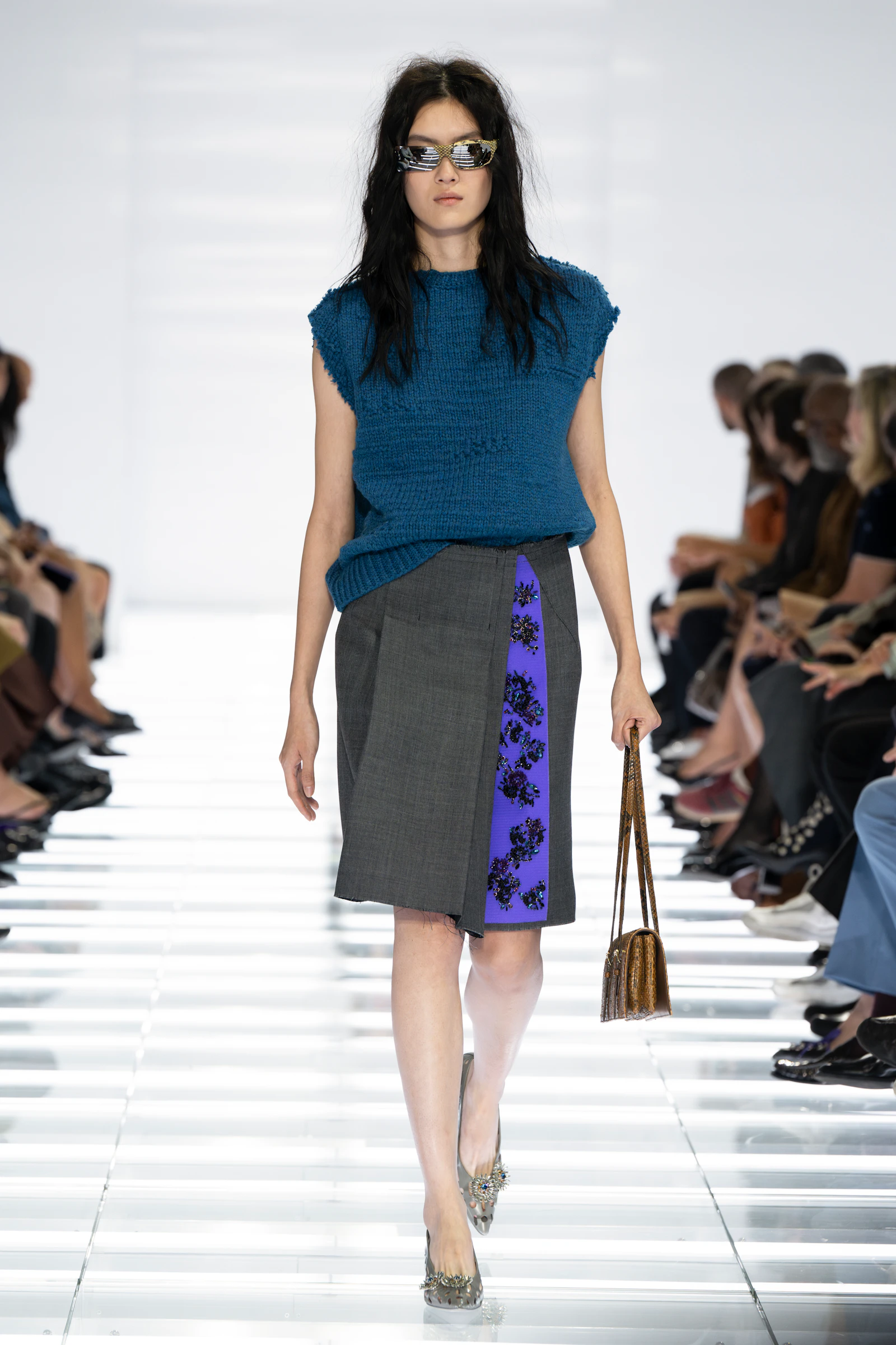 Model in a teal Prada sweater and grey skirt with a purple printed panel
