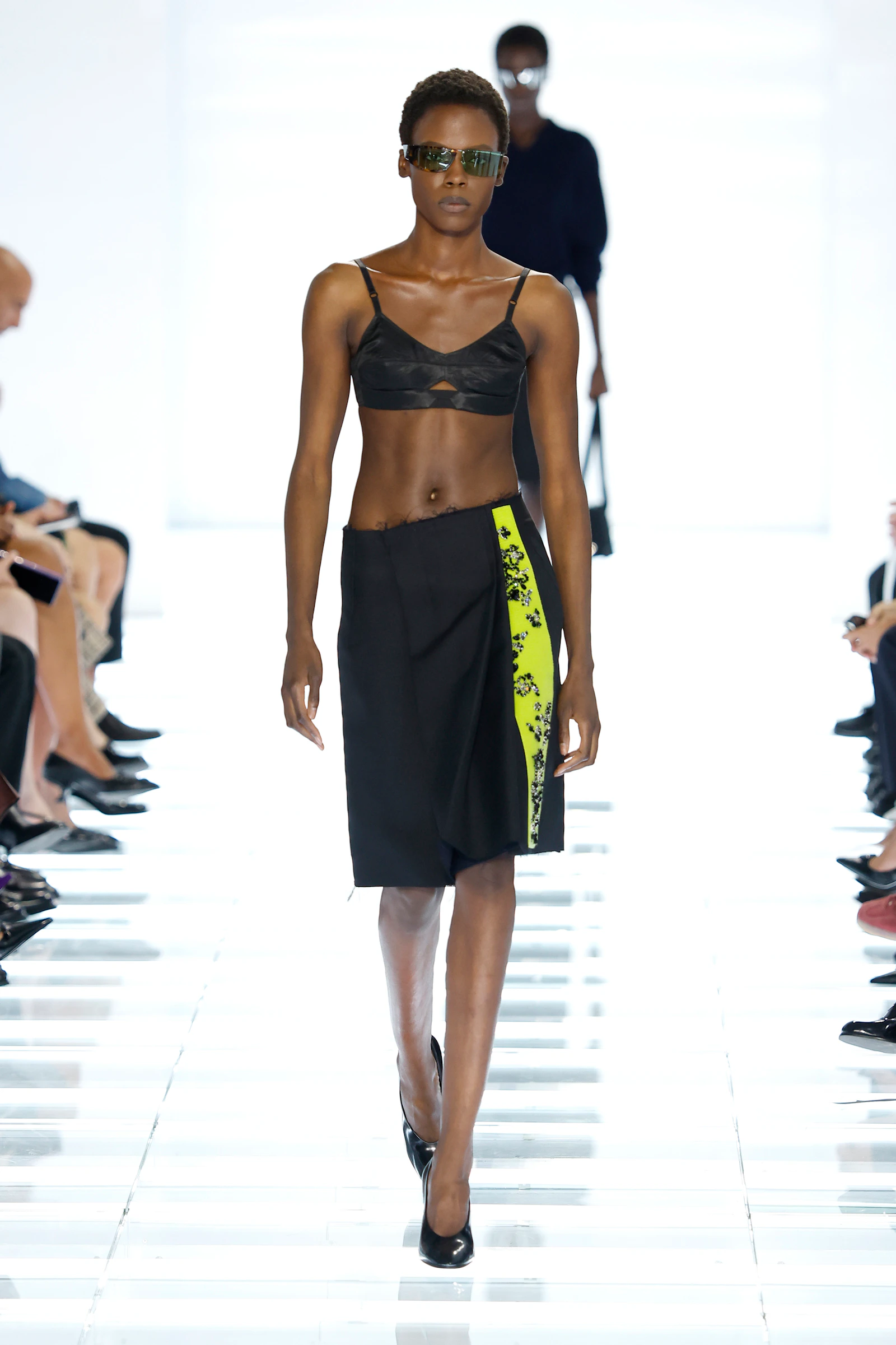 Model wearing a black Prada bra and black skirt with a neon printed slit panel