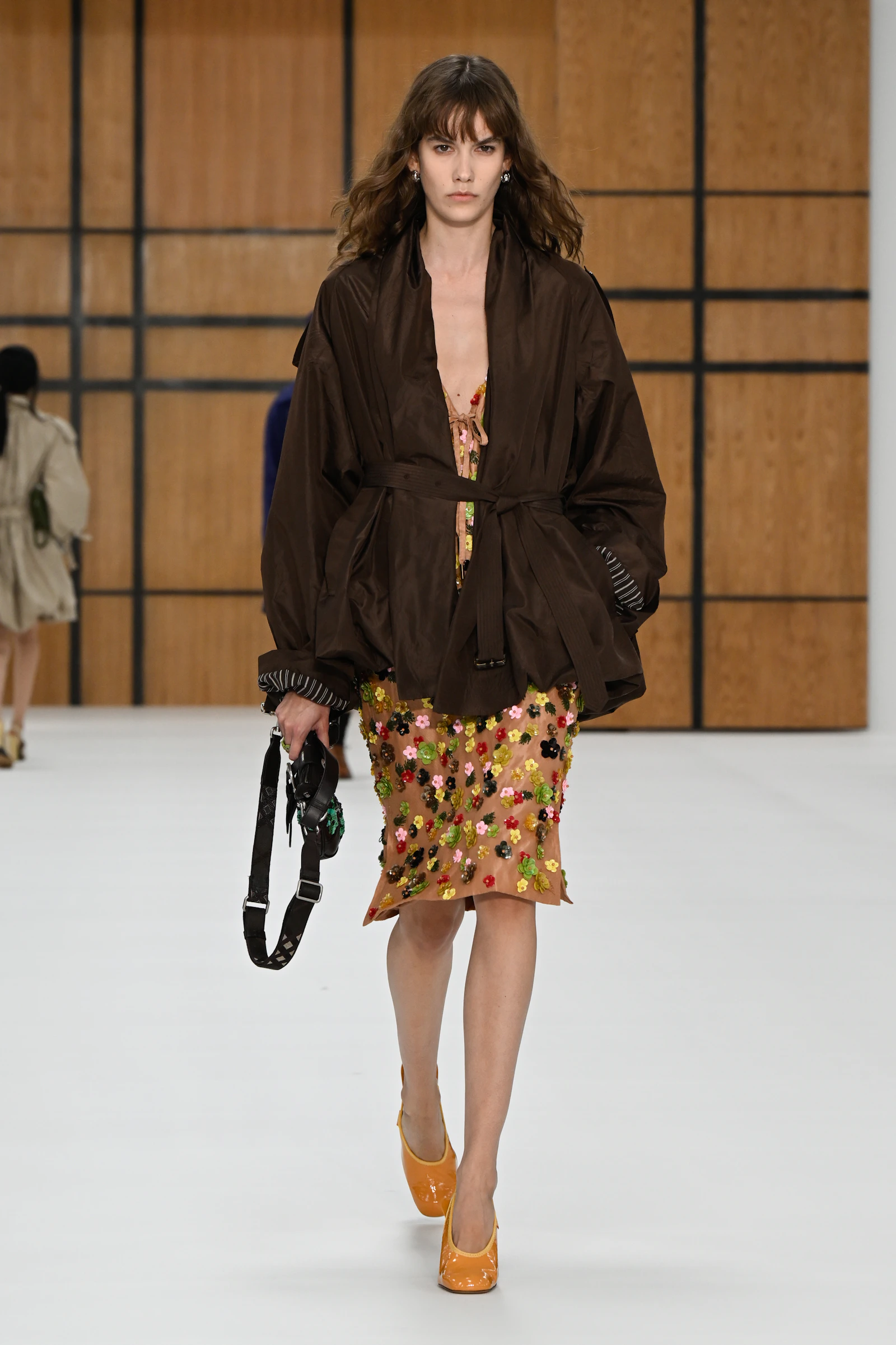 Model wearing a loose dark brown Burberry jacket over a flower-covered skirt