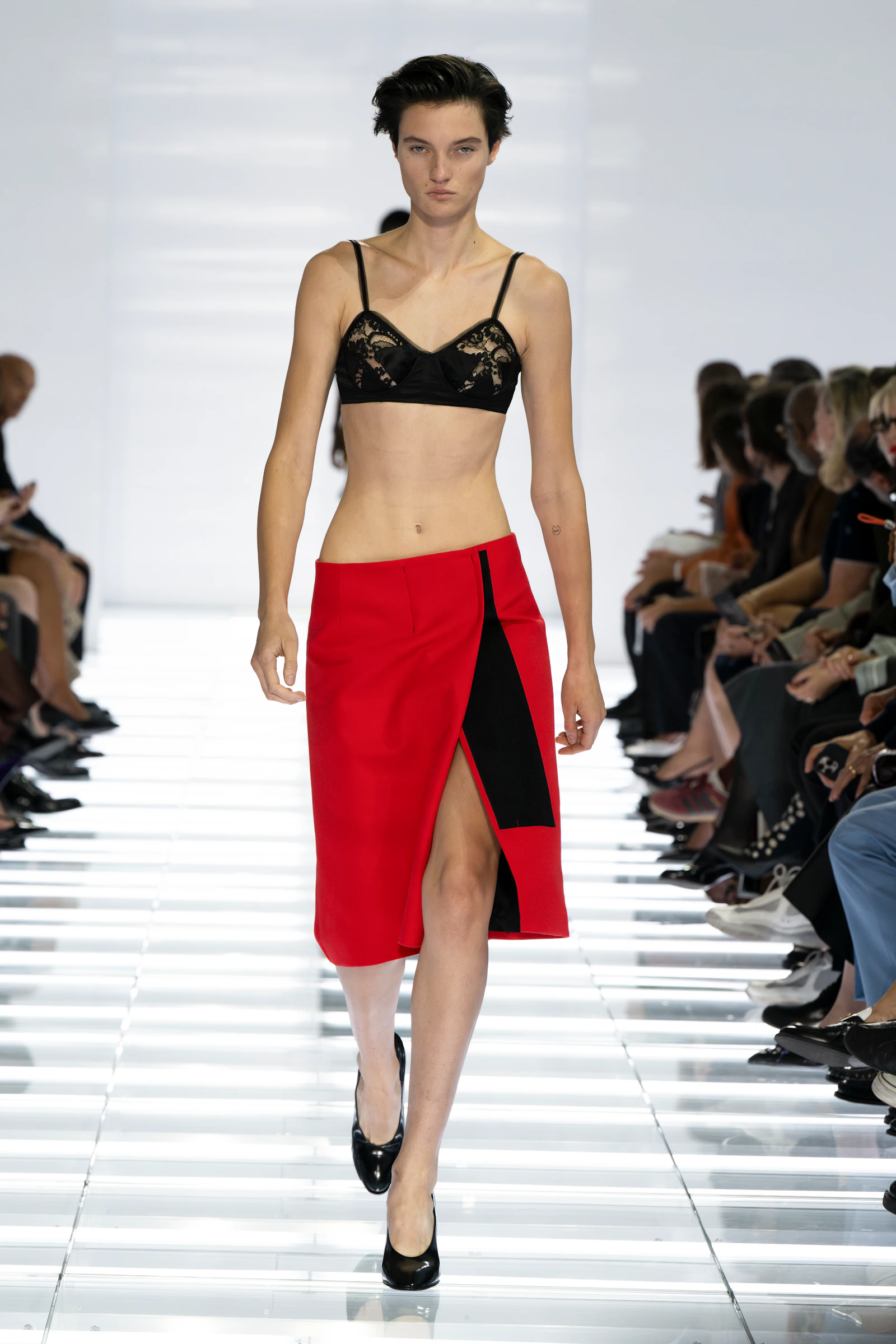 Model wearing a black lace bra with a vivid red high-slit Prada skirt