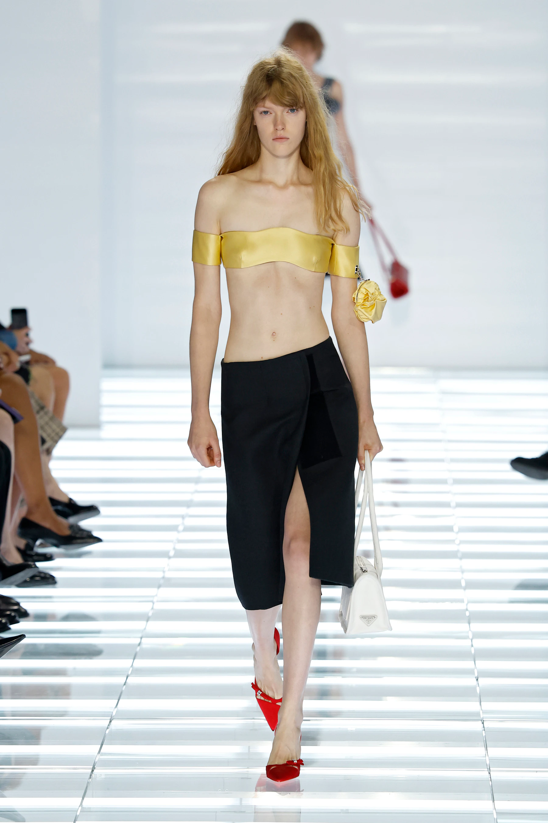 Model wearing a yellow Prada bra top with detached sleeves and slim black skirt-trousers