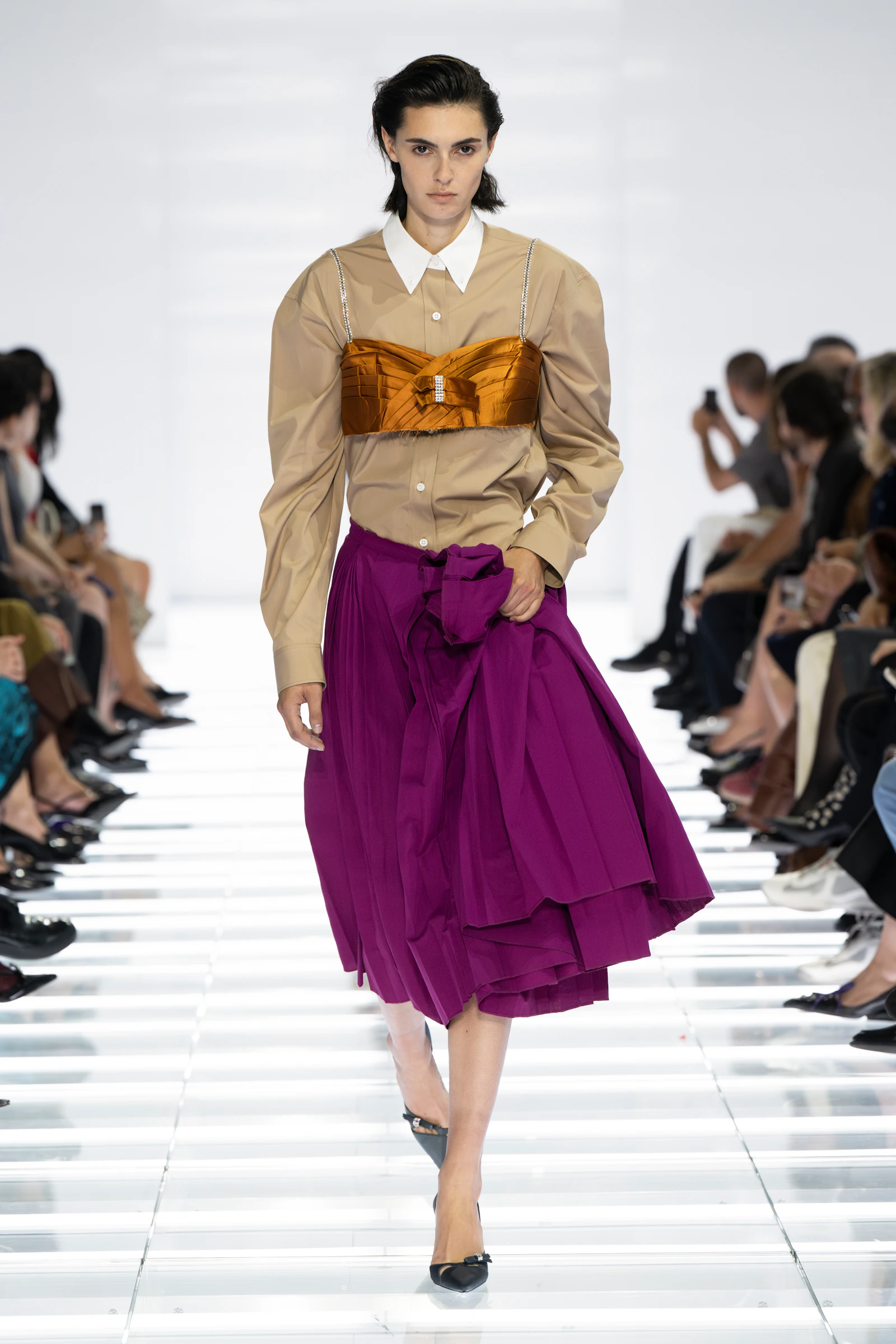 Model wearing a beige Prada shirt, crystal bra and purple pleated skirt