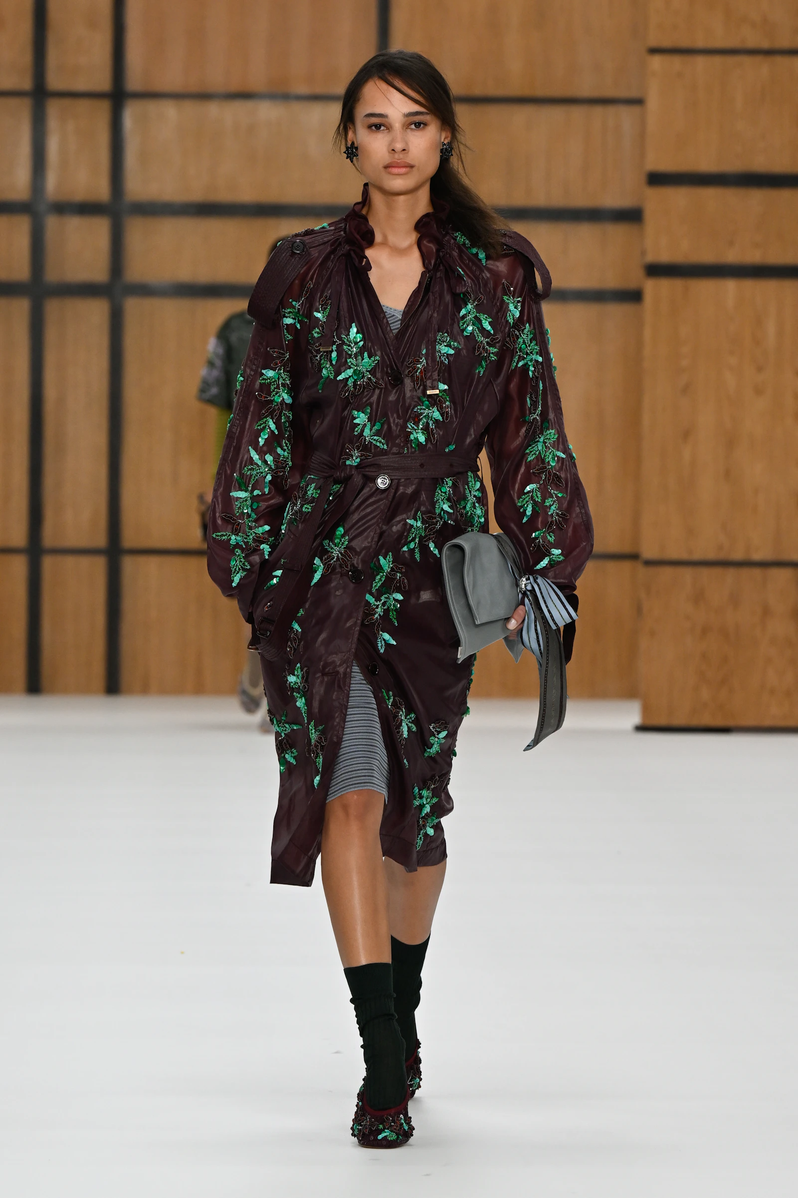 Model in a burgundy Burberry coat embroidered with green flowers and worn with climbing shoes