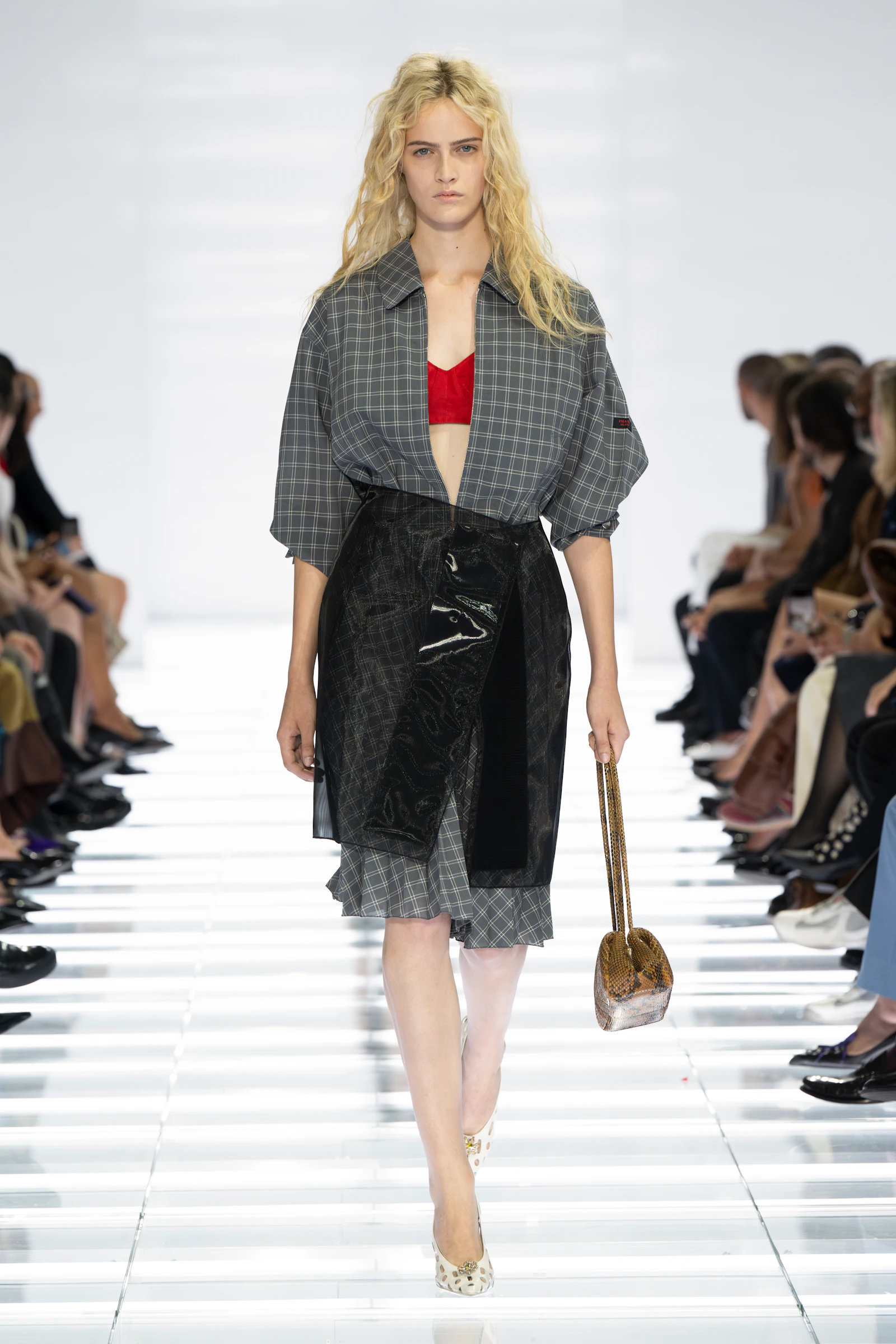 Model in a cropped grey plaid Prada jacket, red bandeau and glossy black layered skirt