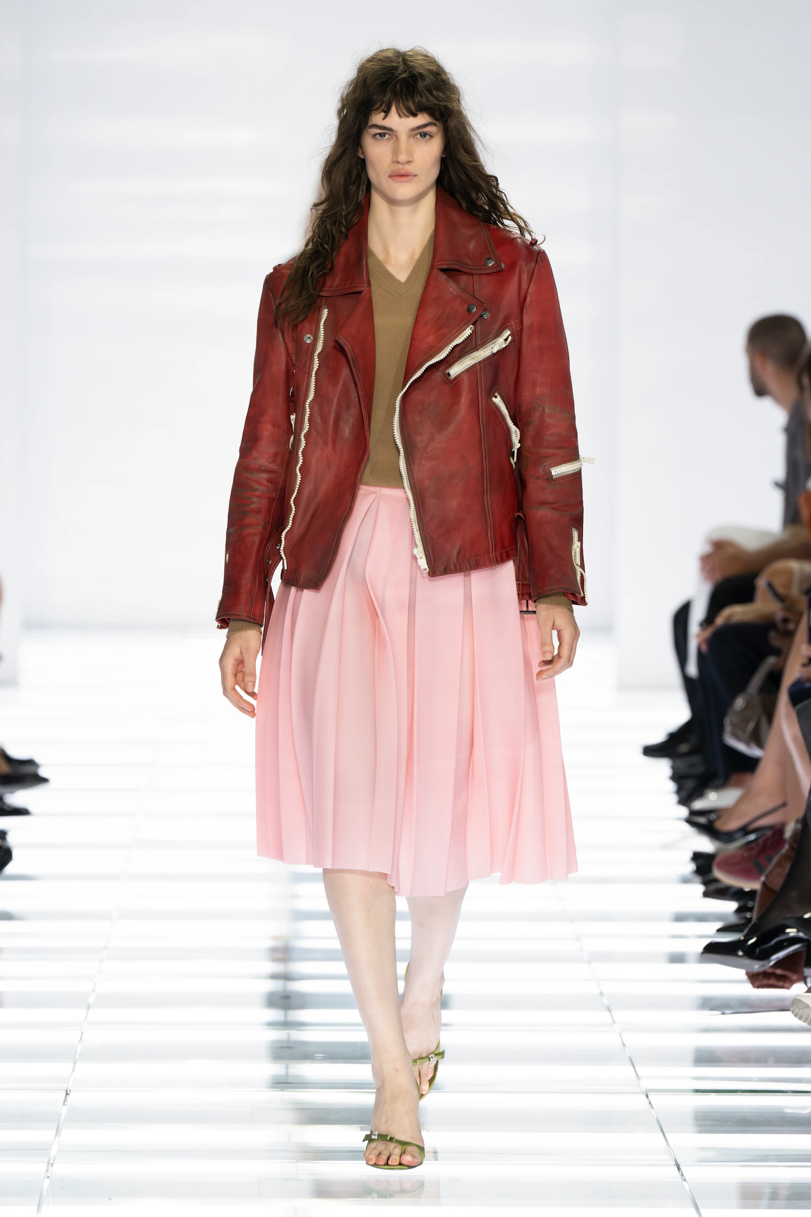 Model wearing a distressed red Prada leather jacket over a pale pink pleated skirt