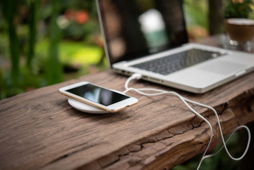 smartphone is charging by wireless charger near lapton on wooden background