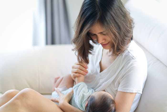 Mother breastfeeding to baby. Young Asian mother giving breast milk to her newborn baby sitting on s...