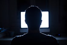 Silhouette of man's head in front of computer monitor light at night