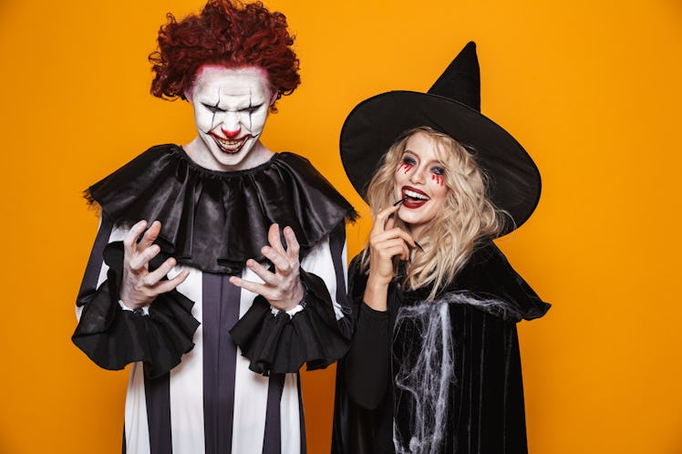 Image of witch woman and clown man wearing black costume and halloween makeup smiling at camera isol...