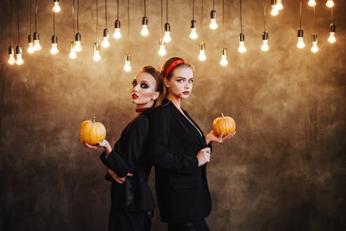 Two happy young women in black witch halloween costumes on dark background