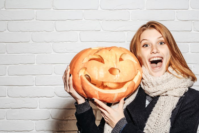 Halloween woman with happy face. Party and traditional food. Woman in coat and scarf at brick wall. ...