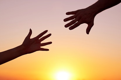 Giving a helping hand.Two hands, man and woman, reaching towards each other at sky sunset.