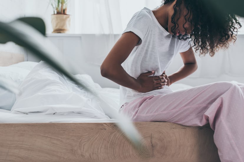 young african american woman suffering from abdominal pain while sitting on bed