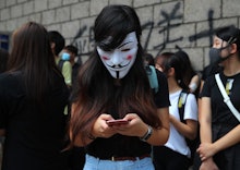 A protester wearing a Guy Fawkes mask uses her mobile phone as protesters supporting activist Edward...