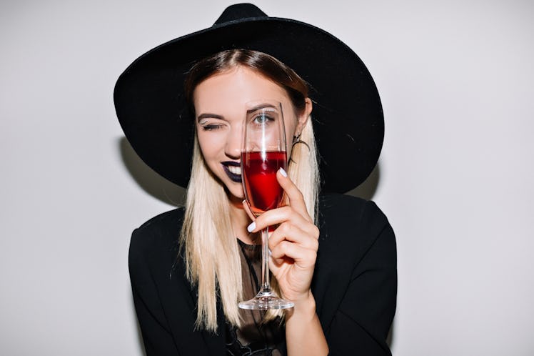 Crazy party time of beautiful woman in elegant black hat with a glass of champagne celebrating new y...