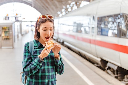 Healthy young woman biting her hamburger at railway station near fast train