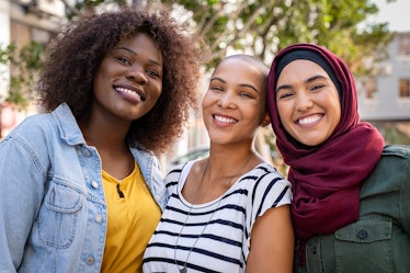 Group of three happy multiethnic friends looking at camera. Portrait of young women of different cul...