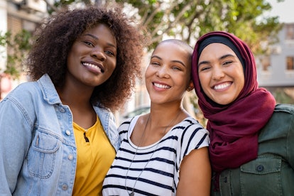 Group of three happy multiethnic friends looking at camera. Portrait of young women of different cul...