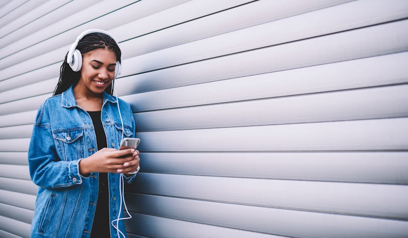 Happy smiling woman enjoying positive audio book via headphones during communicating with friends on...