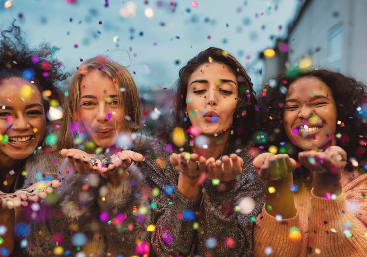 A group of friends blow confetti into the air on New Year's Eve.