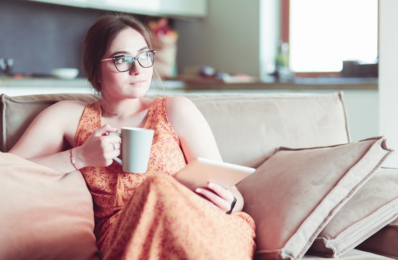 Young woman uses tablet while relaxing at home with coffee on the sofa couch