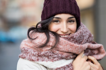 Closeup face of a young happy woman enjoying winter wearing scarf and cap. Smiling girl in a colorfu...