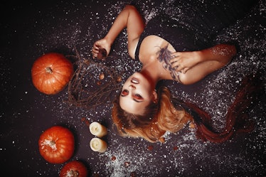 Halloween concept, girl vampire with red eyes red lips lying on floor with pumpkins and snow around....