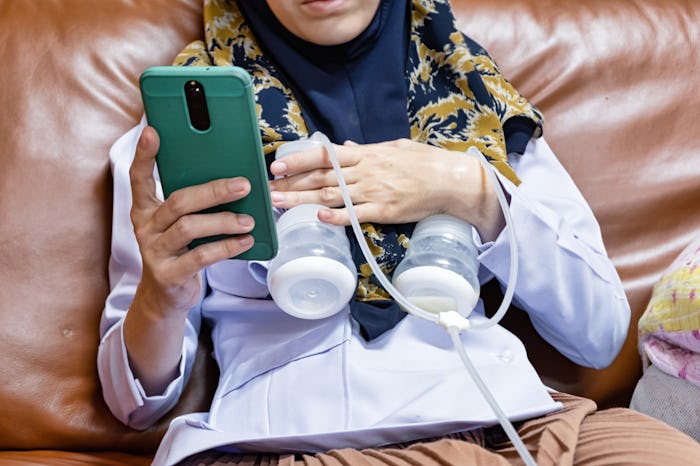 Busy mother playing phone while using automatically electric breast pump feeding for her baby.