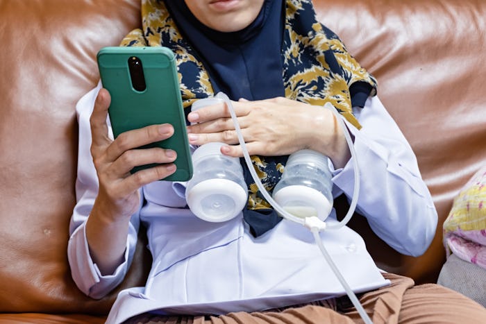 Busy mother playing phone while using automatically electric breast pump feeding for her baby.