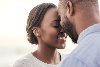 Smiling young African couple standing face to face with their eyes closed while enjoying a romantic ...