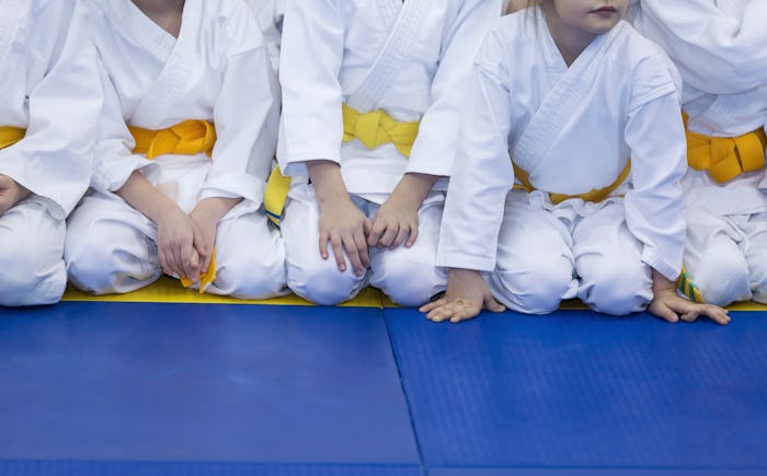 Kids in yellow belts sitting on a blue mat in karate class