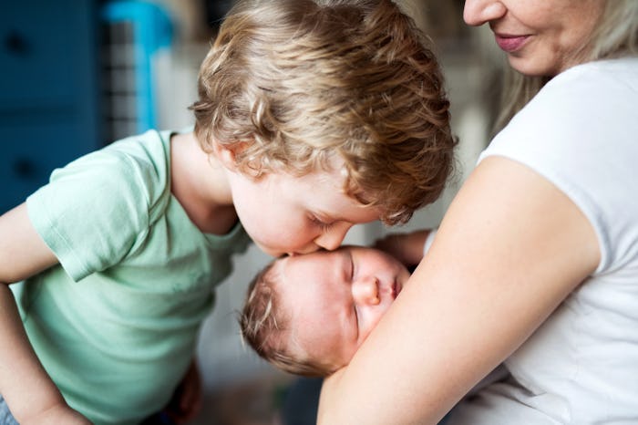 A small boy kissing a sleeping newborn baby brother at home.