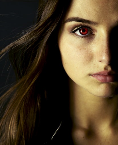 A brunette woman with red eyes is ready to be a vampire for her Halloween costume.