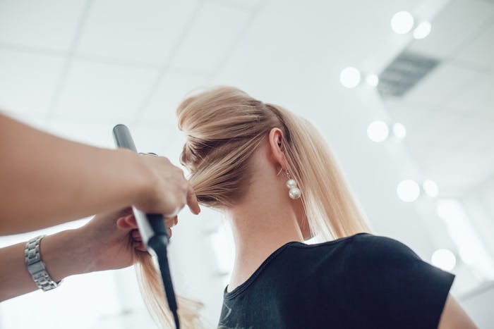 Hair stylist makes a curls for a girl, using hair styling. Hairdresser at work.