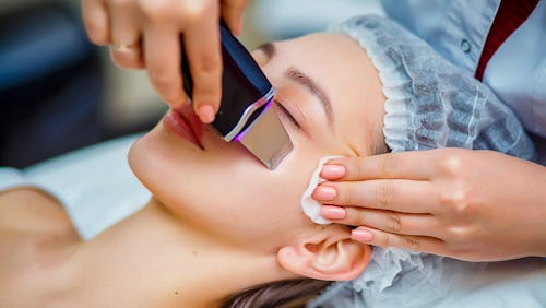 Woman receiving ultrasonic facial exfoliation at cosmetology salon. Procedure clearing clogged pores...