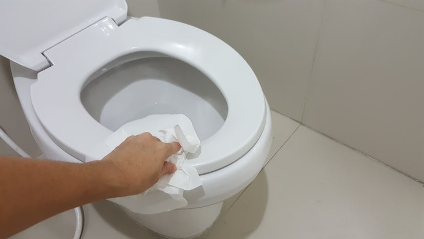Human's hand wipe the toilet seat cover clean with tissue paper.